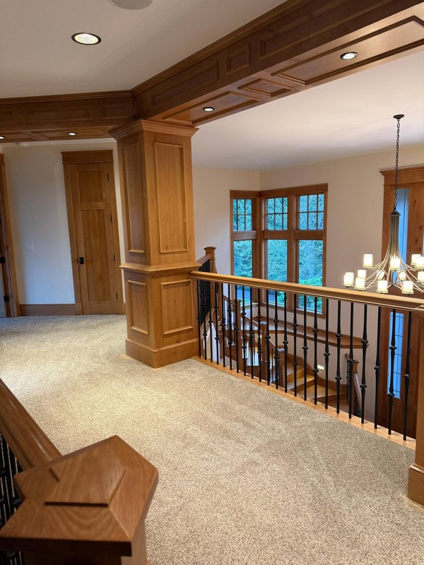 Clean carpeted landing with detailed wood trim, paneled columns, doors, and stair railings throughout the upper level.