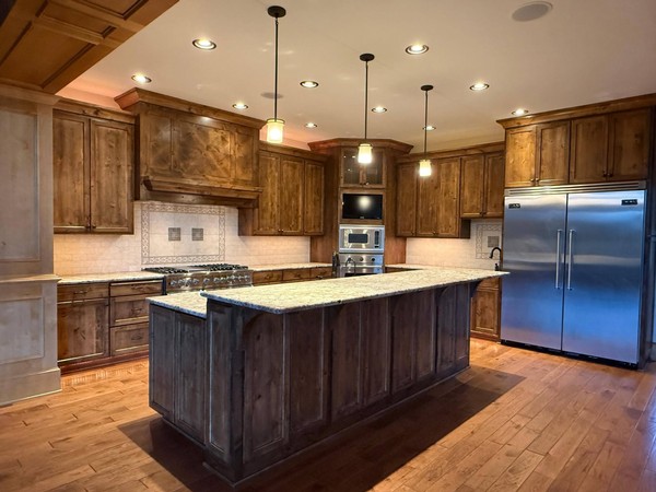 Residential kitchen with clean wood cabinetry, granite countertops, appliances, pendant lights, and hardwood flooring.