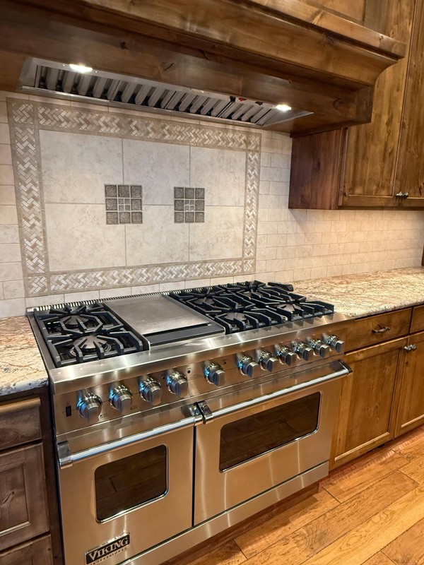Cleaned range area featuring stainless steel appliances, cooktop grates, tiled backsplash, surrounding cabinetry, and countertop surfaces.