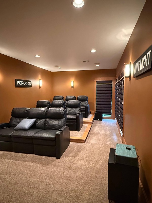 Home theater with clean carpeted flooring, leather seating, wall lighting, window shades, and a dedicated entertainment setup.