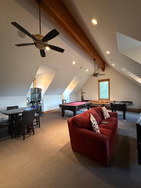 Upper-level recreation room with clean carpet, seating, game tables, ceiling fans, skylights, and bright finished surfaces.