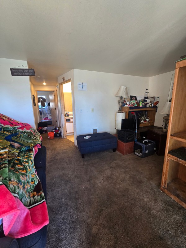 Residential living area with furniture, personal belongings, bedding, and household items arranged throughout the room.