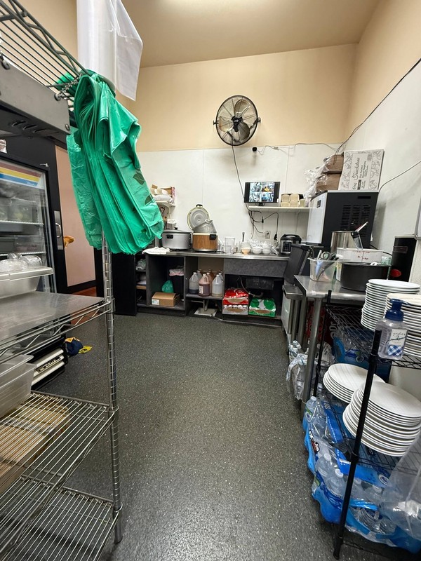Organized restaurant service and storage area with kitchen equipment, shelving, dishware, and supplies arranged throughout the workspace.