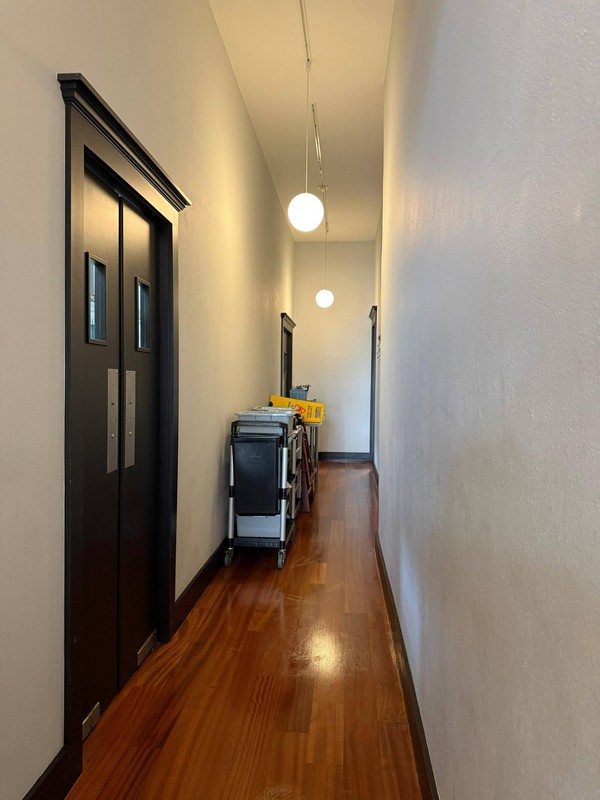 Clean hallway connecting the restaurant&rsquo;s interior spaces, with polished wood flooring, illuminated fixtures, and a cleaning cart positioned for service.