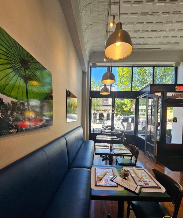 Dining area with cleaned tables, menus, seating, pendant lights, artwork, and front entry glass arranged for restaurant service.