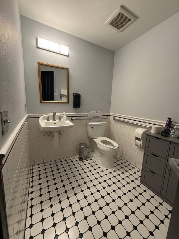 Restaurant restroom with cleaned sink, mirror, toilet, tiled walls, and patterned floor ready for continued customer use.
