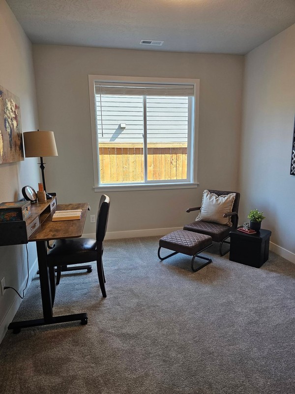 The home office and sitting area are organized and refreshed, with the desk, chair, window area, and carpeted floor presented neatly.