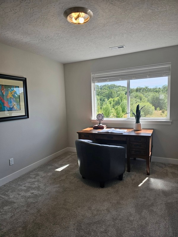 A second office space appears clean and uncluttered, with the desk, chair, carpet, window, and surrounding surfaces ready for comfortable use.